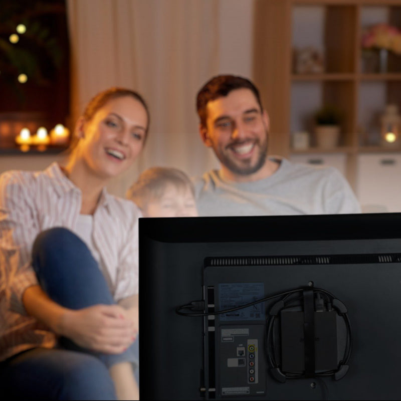 Photo of a woman, child, and man watching TV with a Wrap Caddy holding an Amazon Fire TV attached to the back of TV.