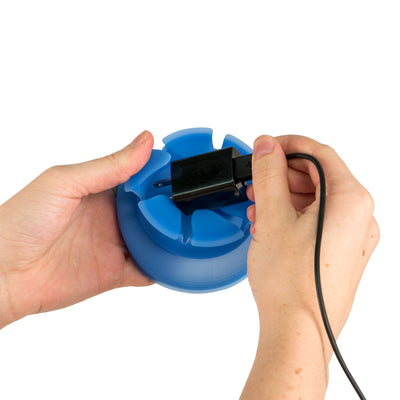 Photo of two hands demonstrating how to insert a power brick and cord into a blue NestXL.