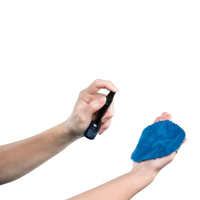 Studio photo of a hand holding  a 0.5 fl. oz. bottle of ScreenDr and spraying solution on a blue microfiber cloth being held by the other hand.